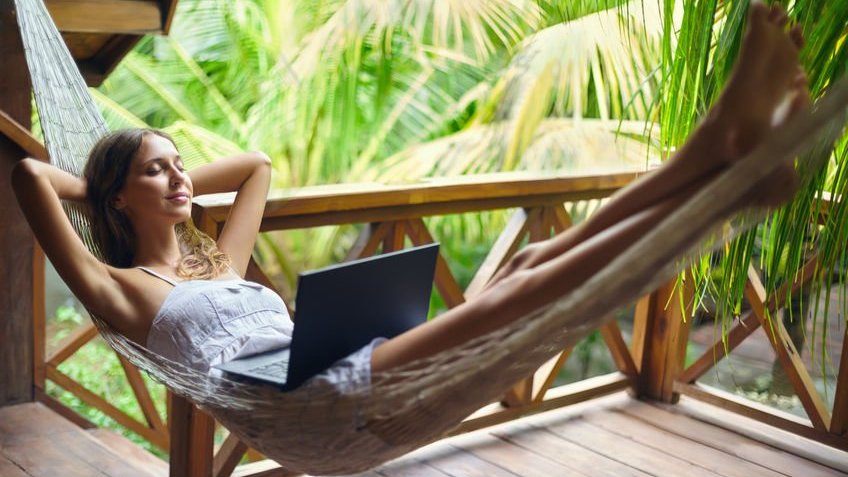 Mulher relaxando em uma rede com o laptop no colo.