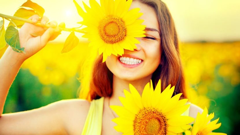 Garota sorrindo com girassóis em frente o rosto e sol refletindo