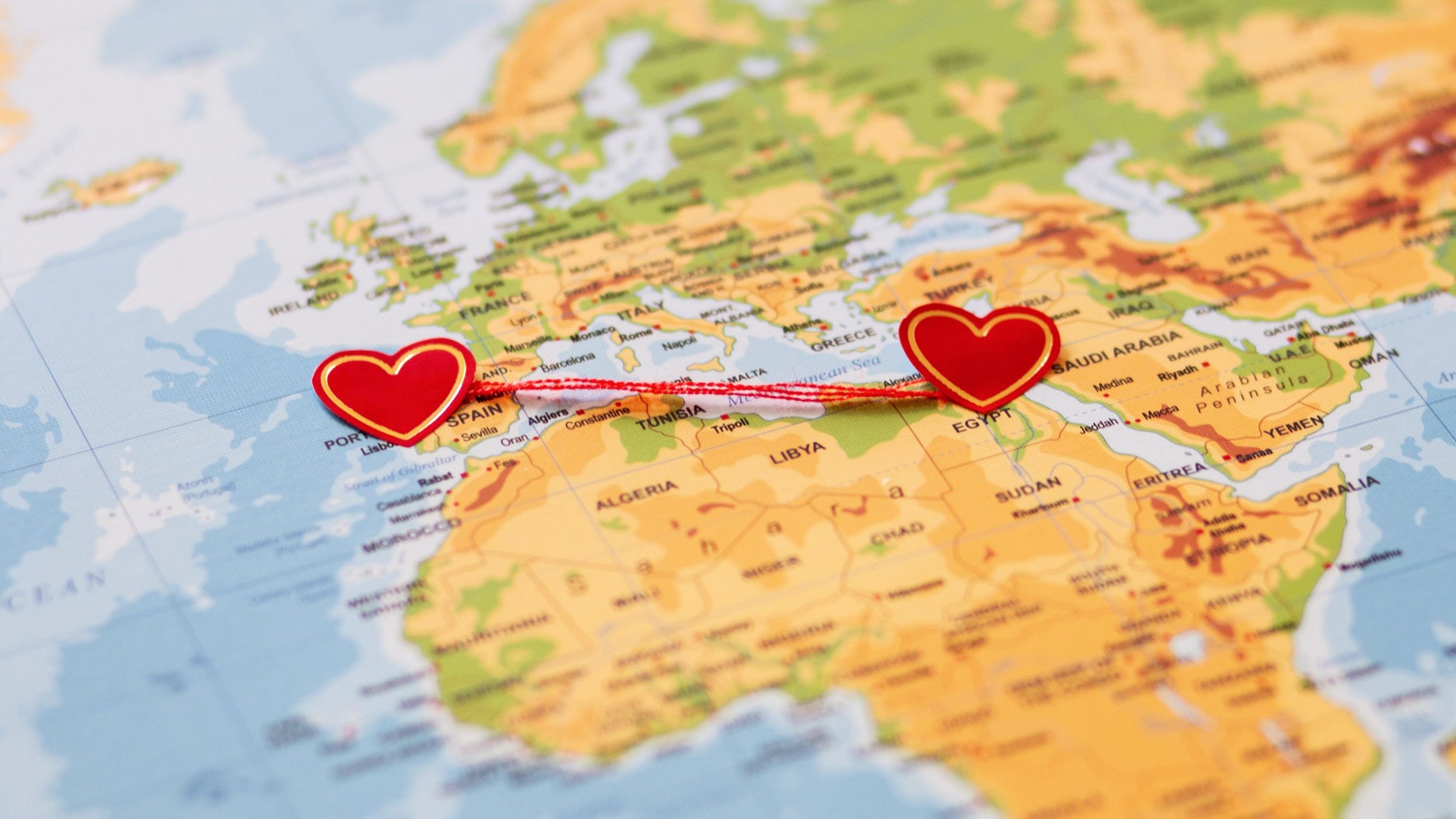 Um mapa da Europa e África, com dois corações em países diferentes. Esses corações são ligados por um fio vermelho.