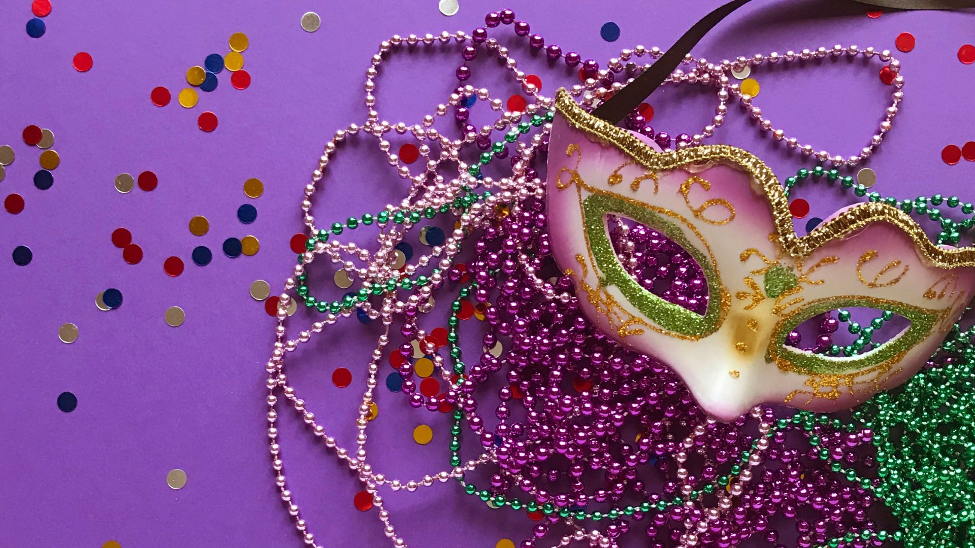 Máscara de carnaval no fundo roxo com confetes e colares coloridos de conta