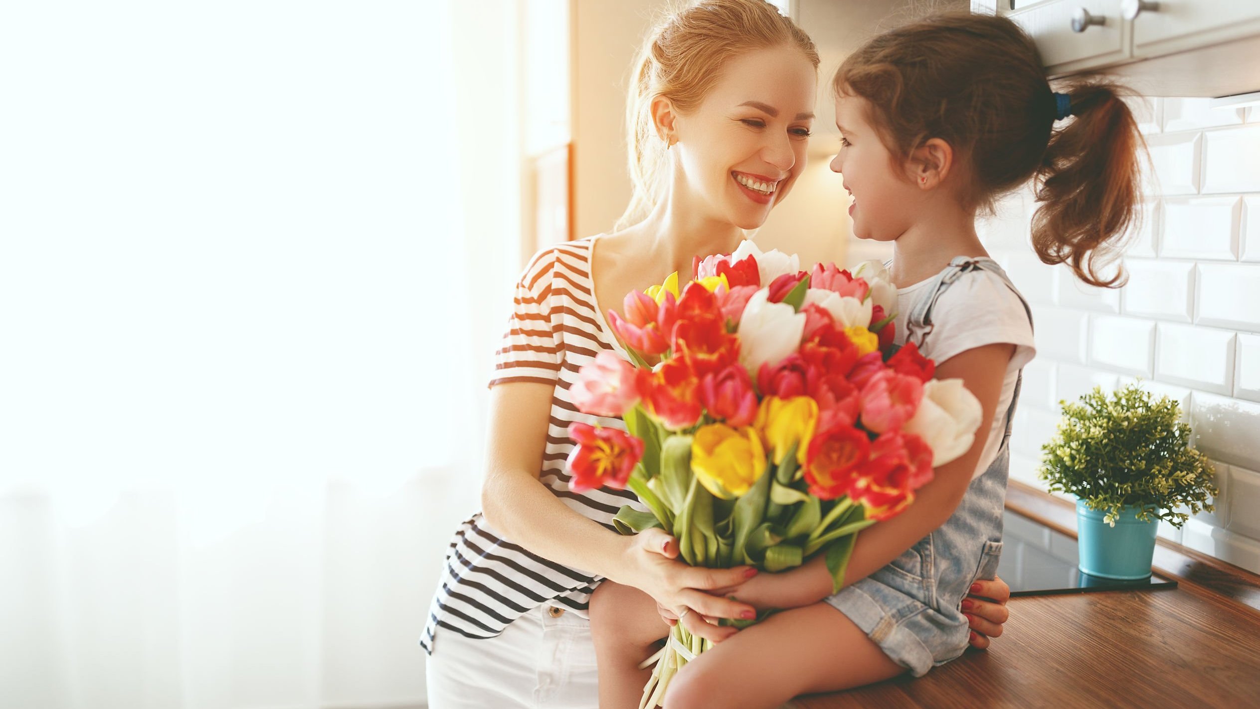 Mãe e filha brancas com buquê de flores nos braços e expressões felizes.