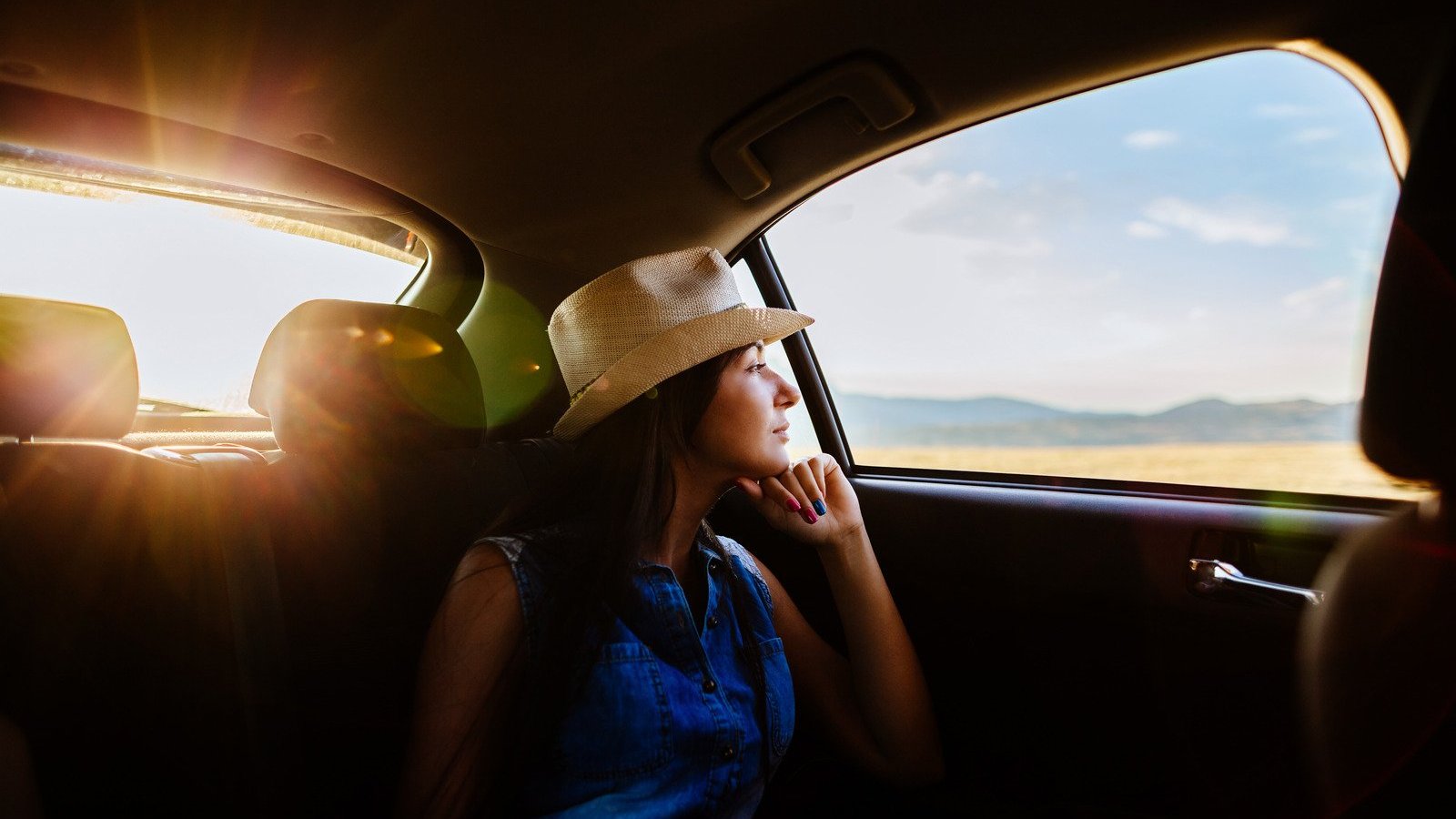 Mulher usando chapéu dentro de um carro, olhando para a janela.