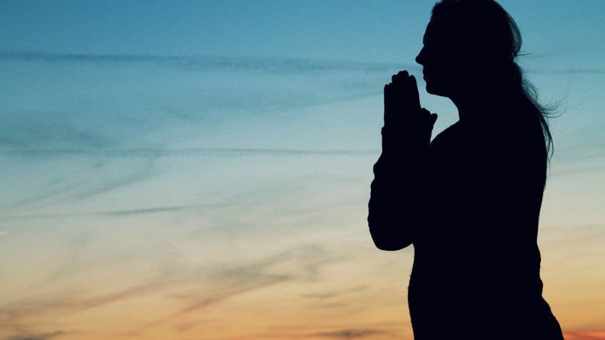 Silhueta de mulher rezando durante o pôr-do-sol.