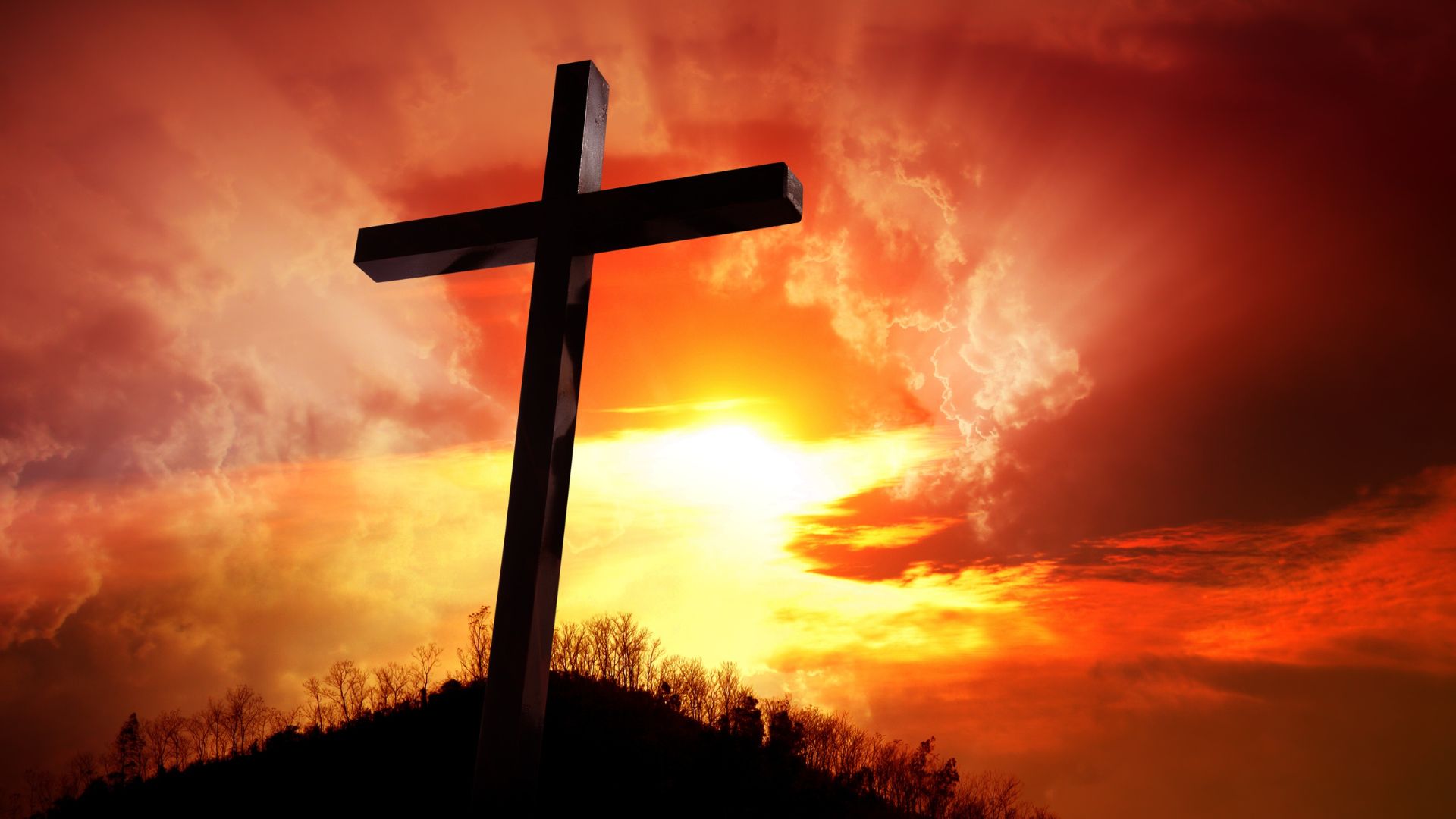 Imagem de um lindo pô do sol de cor alaranjado, com uma cruz de madeira sobre um monte.