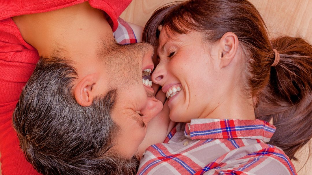 Sunemotion / Getty Images / Canva Homem e mulher deitados ao contrário com o rosto encostado um no outro, sorrindo