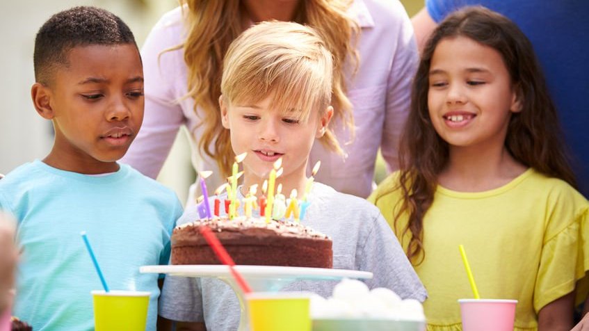 Criança em frente a bolo de anivrsário e outras crianças em volta