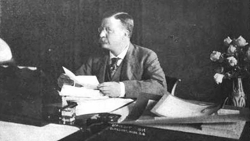 Presidente americano Theodore Roosevelt sentado em mesa, segurando papel