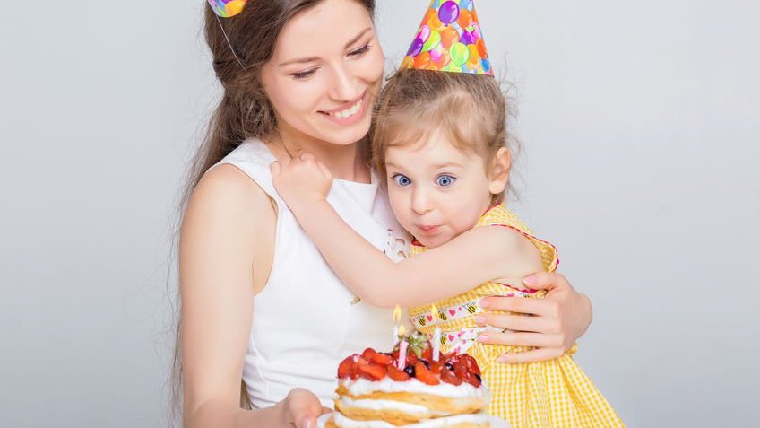 Mulher segurando criança no colo e bolo de aniversário