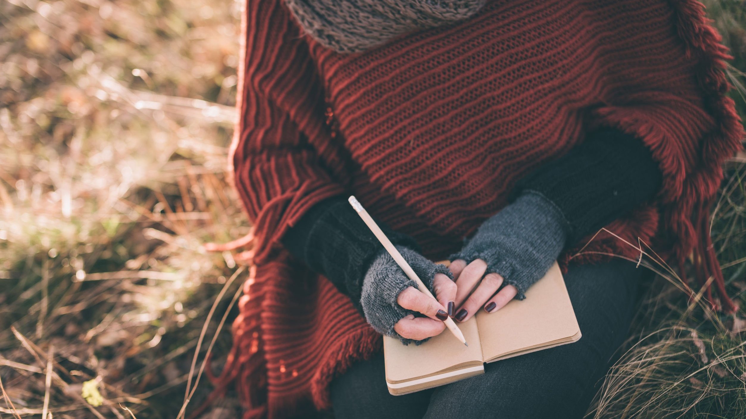 Mulher escrevendo em um caderno sentada no gramado