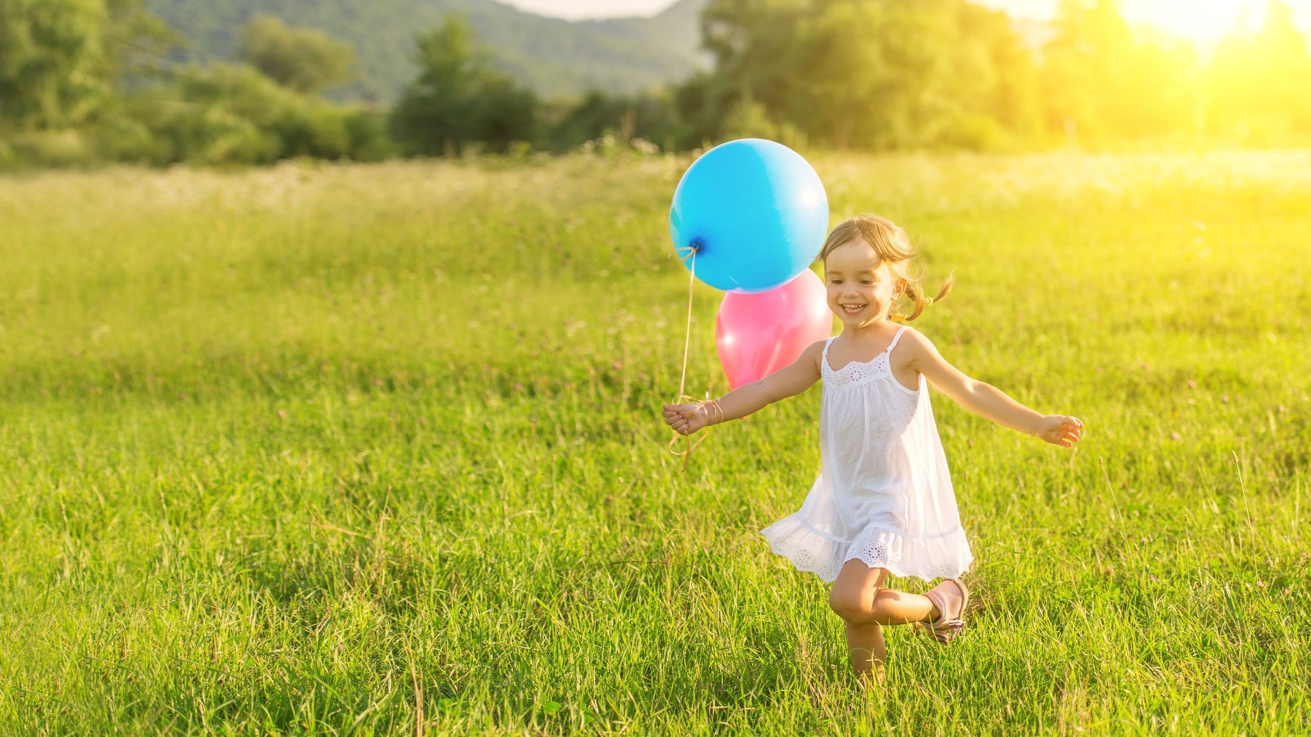 Menina pequena correndo em um campo enquanto segura balões de aniversário.