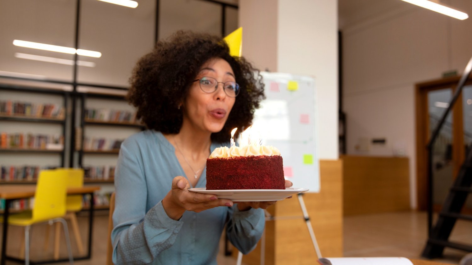 Mulher negra usando um chapéu de aniversário enquanto assopra as velas do bolo