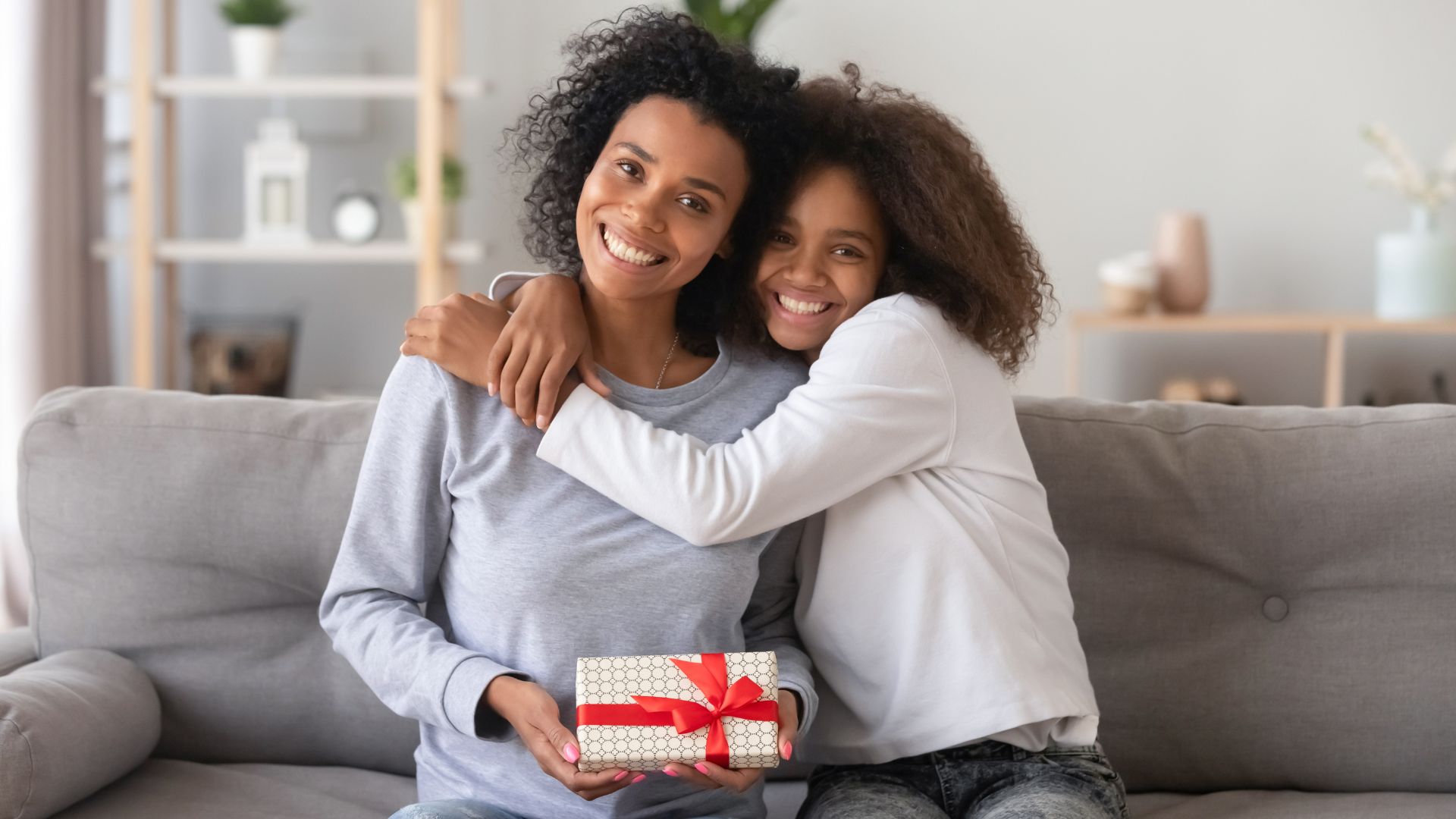 Imagem de uma filha abraçando sua mãe que está segurando um presente