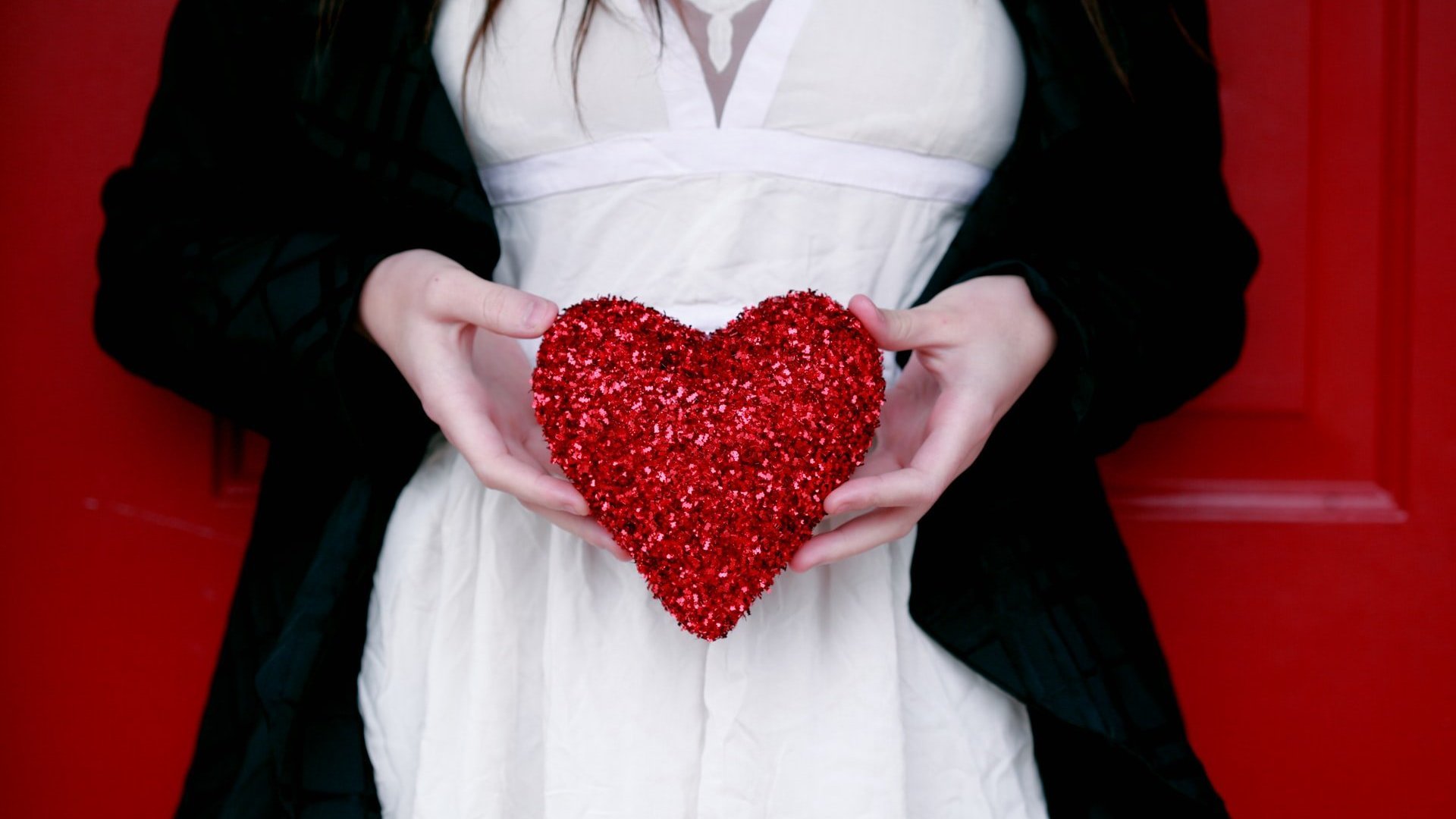 Mulher branca segurando coração vermelho de glitter.