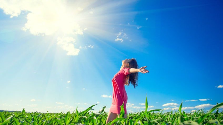 Mulher de braços abertos sendo iluminada pelo Sol