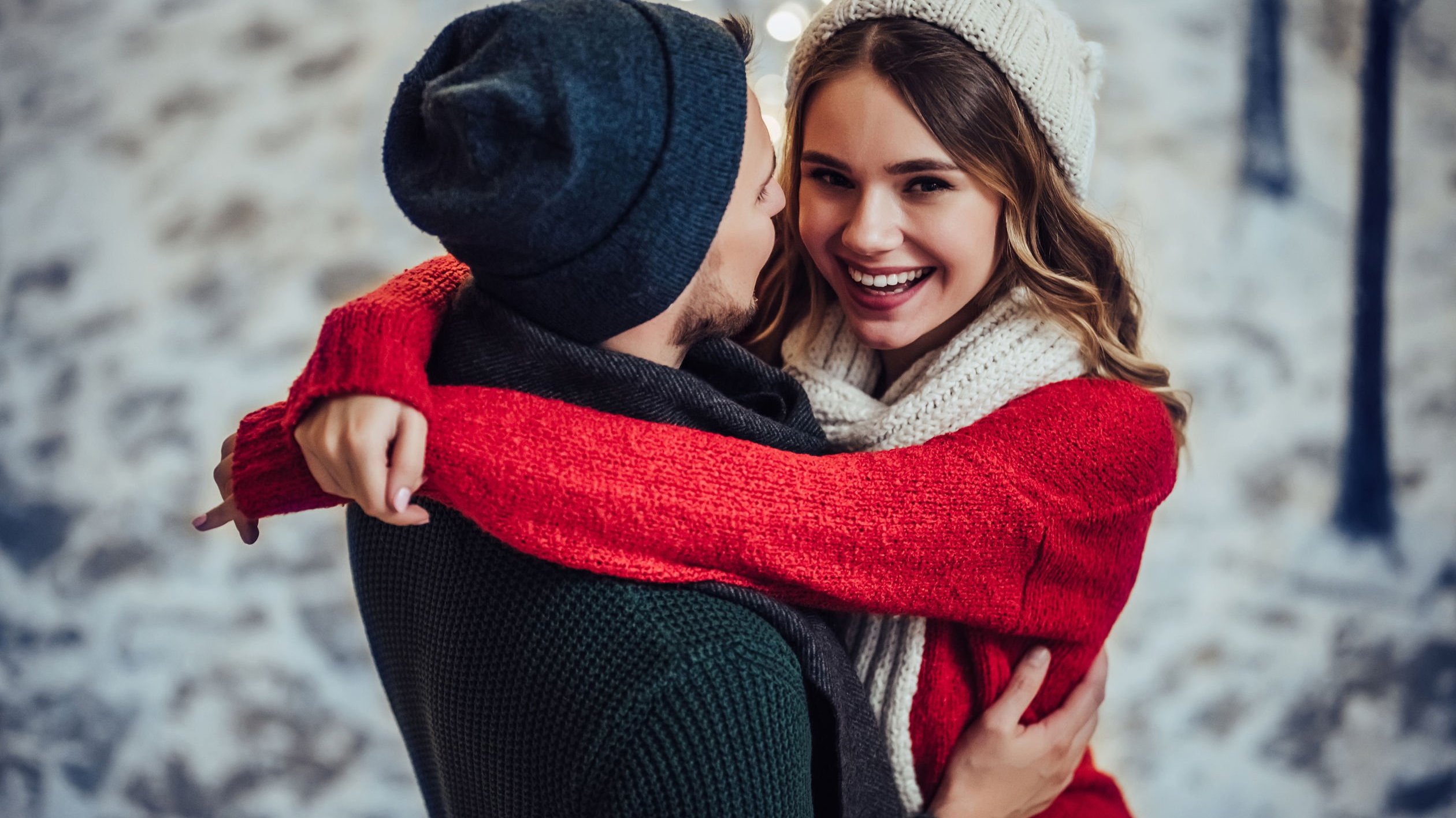 Homem e mulher brancos se abraçando, vestindo roupas de inverno.