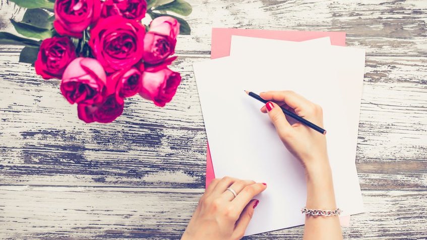 Pessoa escrevendo carta com rosas ao lado