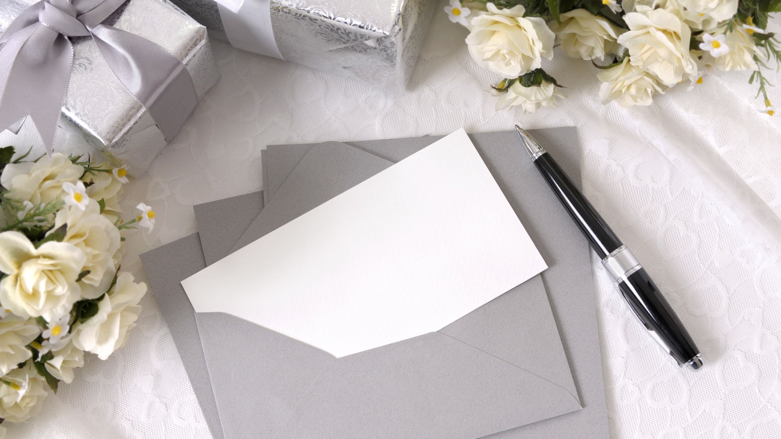 Envelopes com convites em branco em uma mesa, ao lado de flores e presentes.