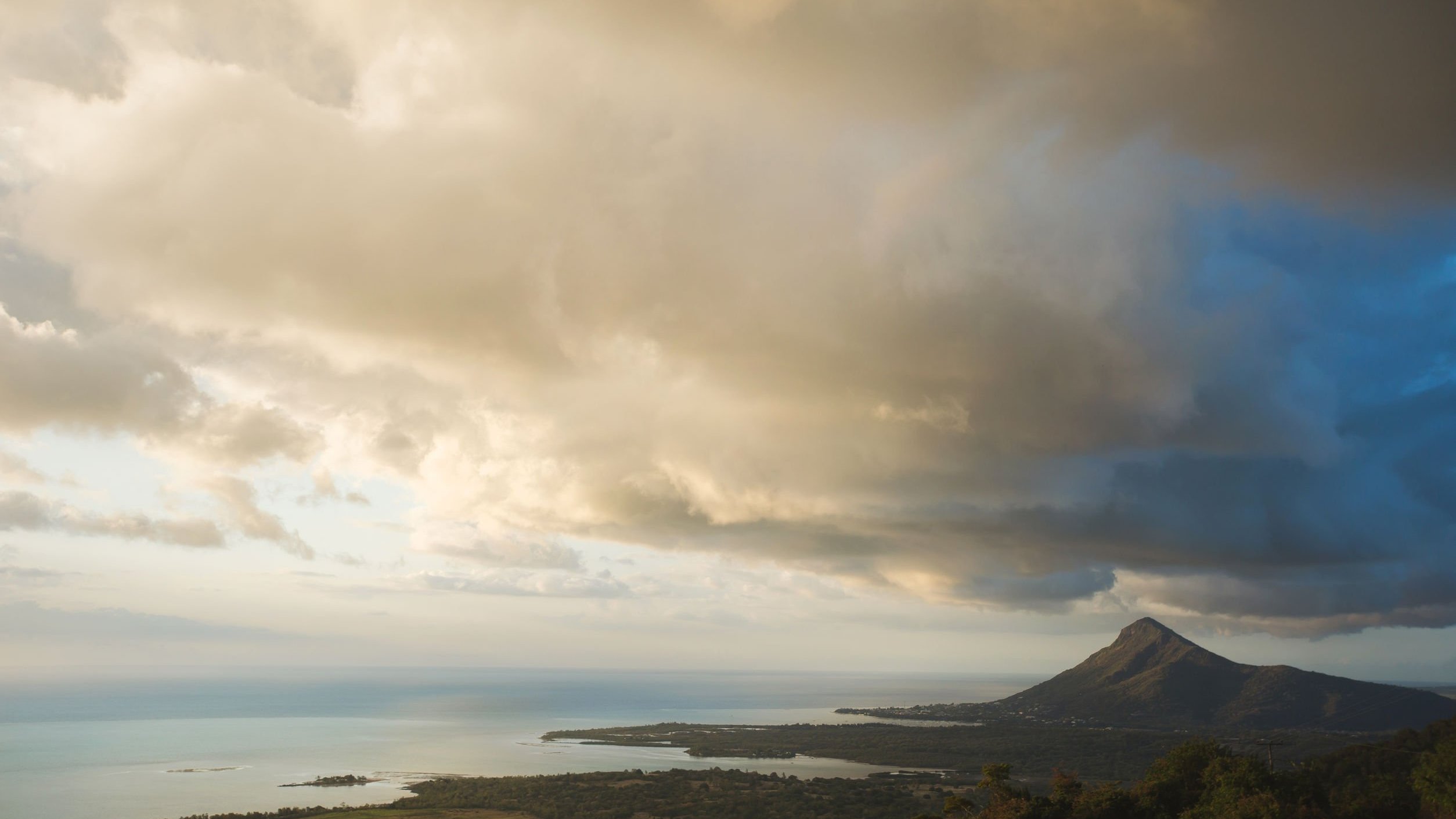 Céu com nuvens, vistas de uma montanha alta, com vista para outras montanhas e para o mar.