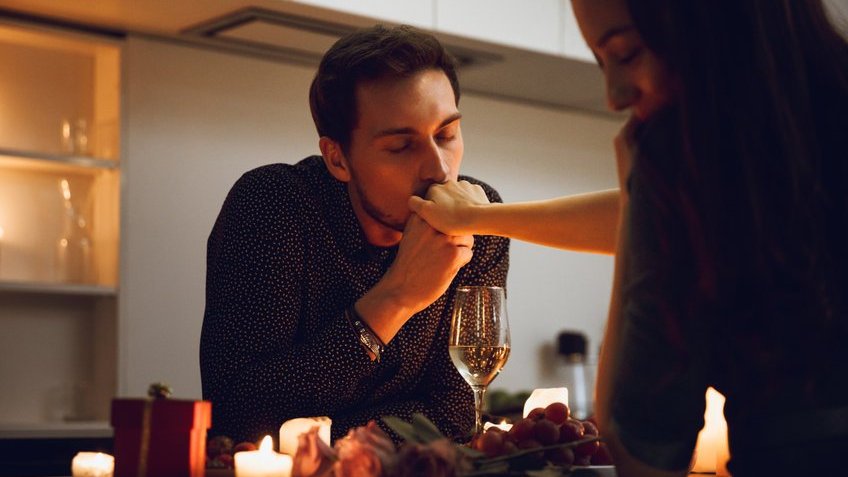 Homem beijando a mão de uma mulher durante jantar