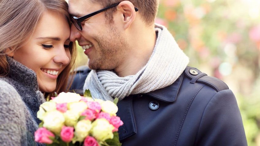 Casal feliz se abraçando segurando flores na cidade.