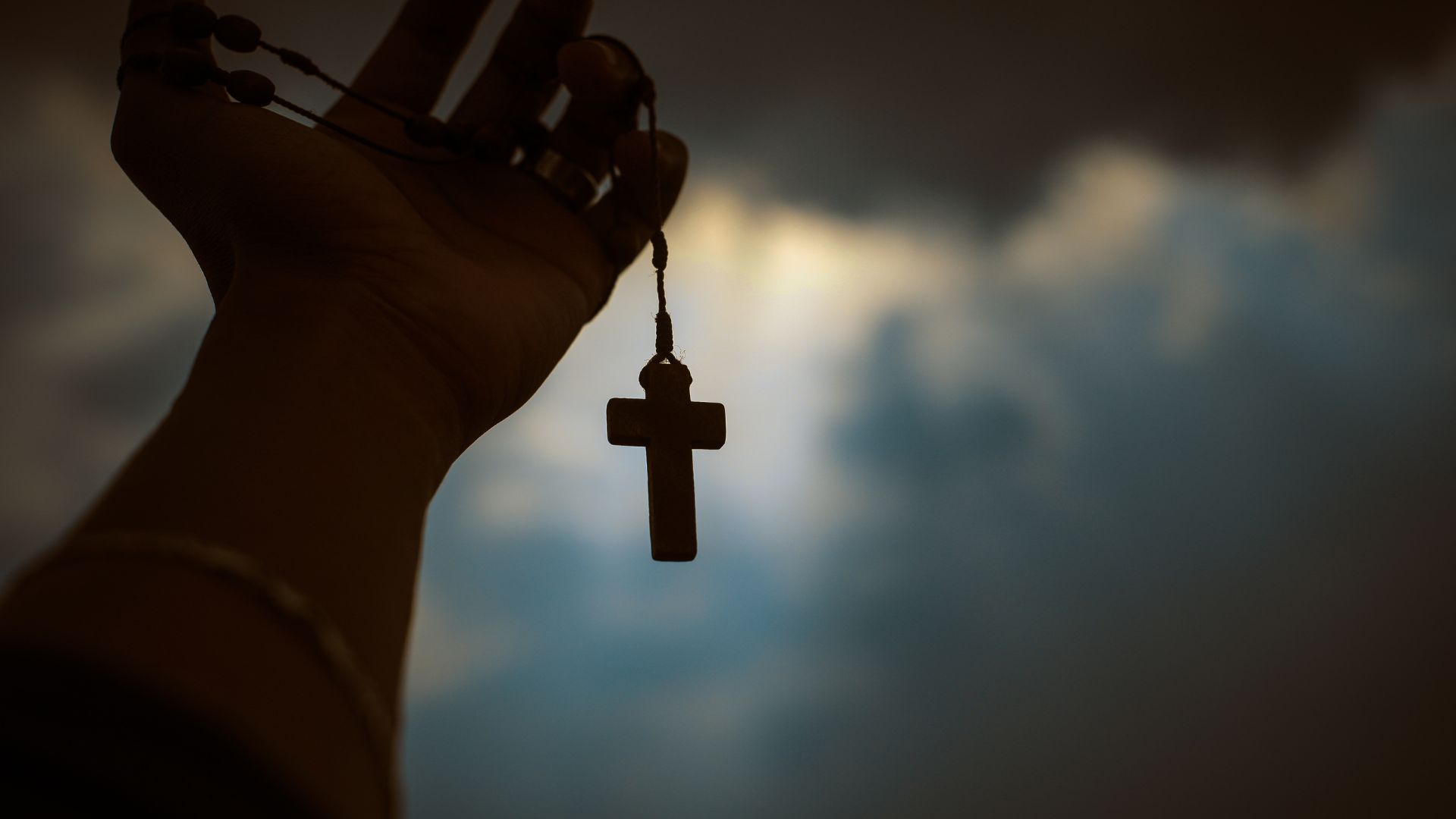 Imagem de uma mão segurando uma cruz de madeira.