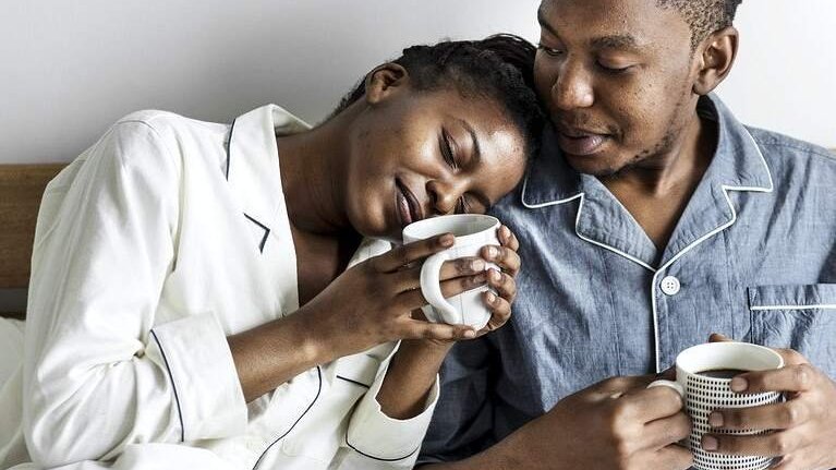 Mulher deitada em ombro de namorado segurando xícara de café