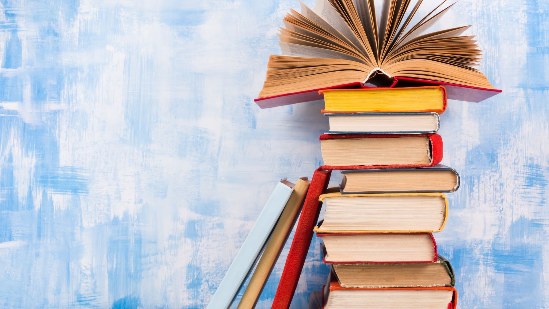 Vimvertigo de Getty Images pro para o Canva Imagem de fundo azul claro. Em destaque temos uma pilha de livros que são indicados para leitura durante o período do Natal.