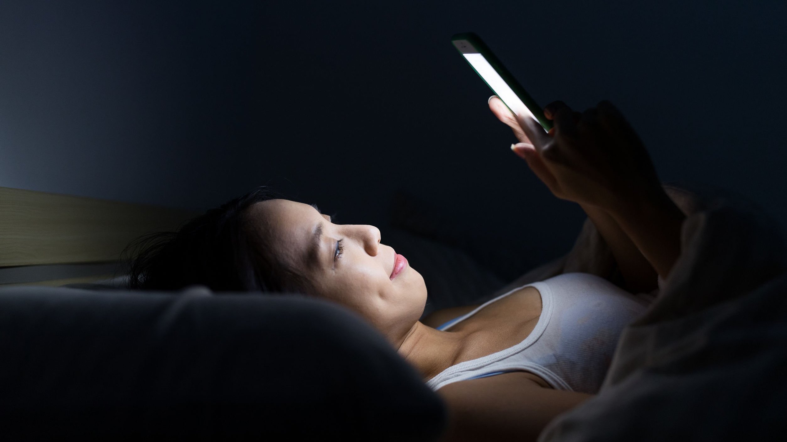 Mulher deitada na cama sorrindo olhando para celular