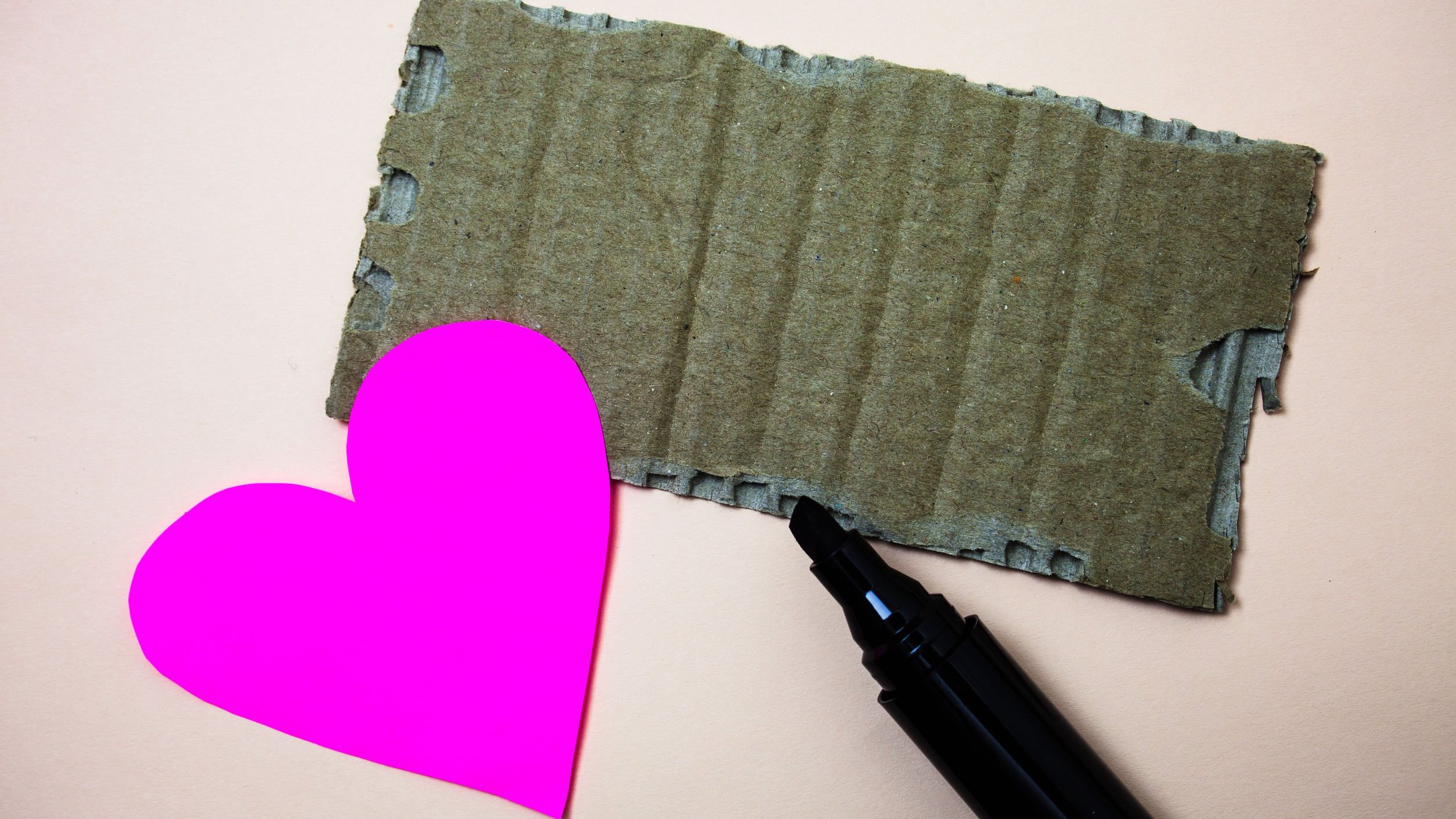 Coração de papel rosa ao lado de pedaço de papelão e canetinha preta