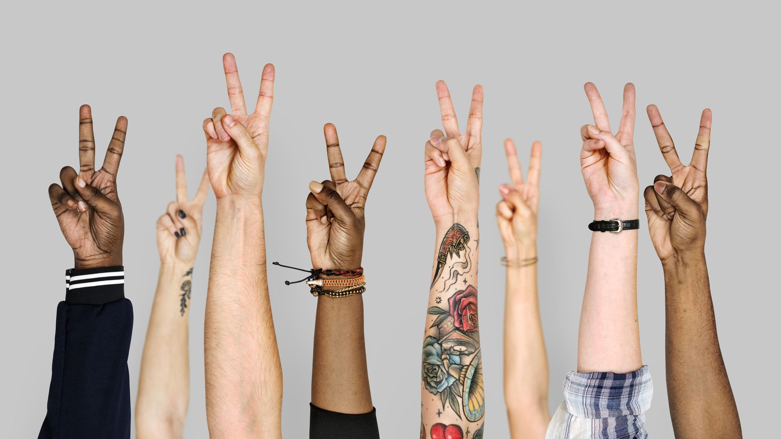 Braços de diversas pessoas levantados com os dedos formando o símbolo de paz e amor