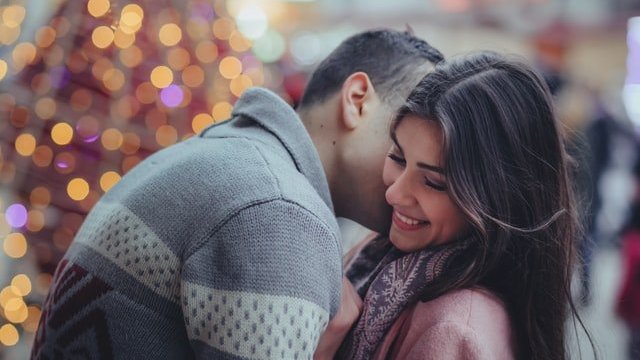 Mulher sorrindo enquanto homem beija seu pescoço