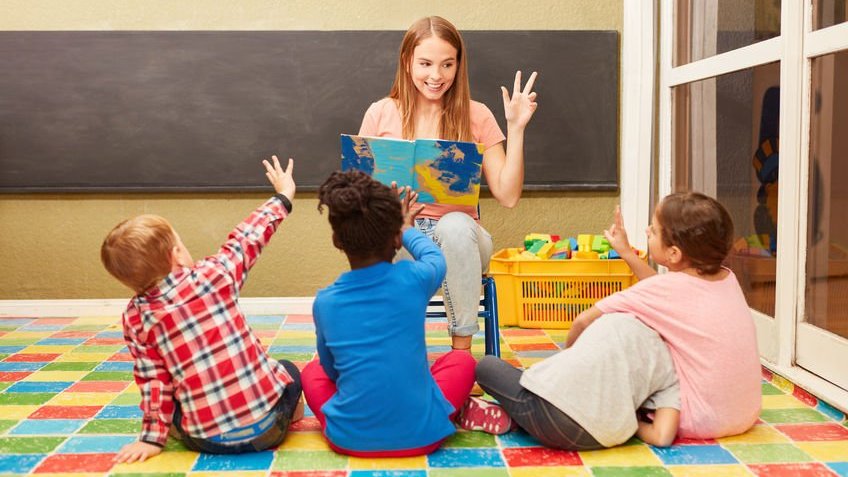 Professora e as crianças se divertem juntas enquanto lêem em voz alta no jardim de infância