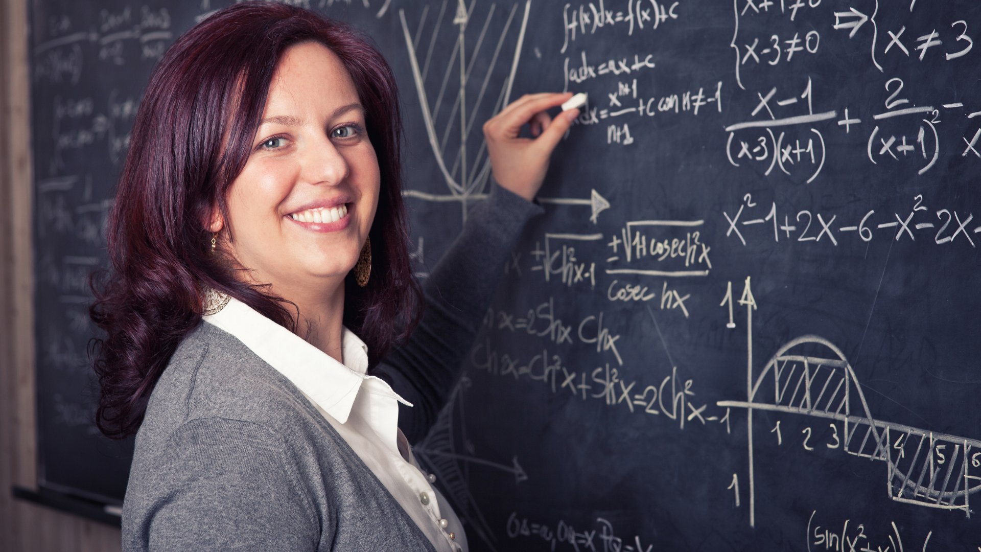 Professora escrevendo na lousa e sorrindo