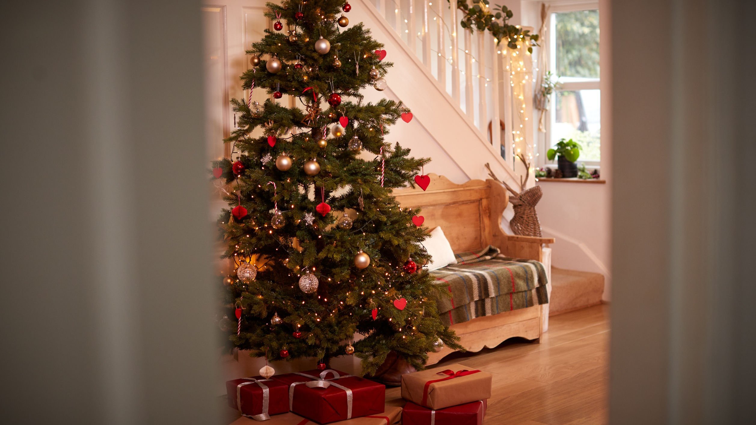 Árvore decorada com enfeites natalinos. Abaixo dela, há presentes.