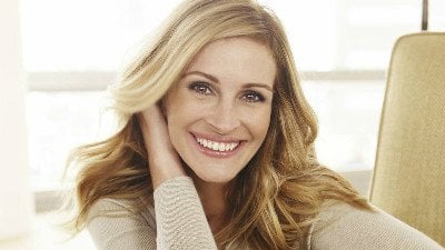 People Magazine Julia Roberts sorrindo para a câmera durante ensaio de fotos. Sua mão direita está embaixo do seu cabelo, encostando em sua orelha.