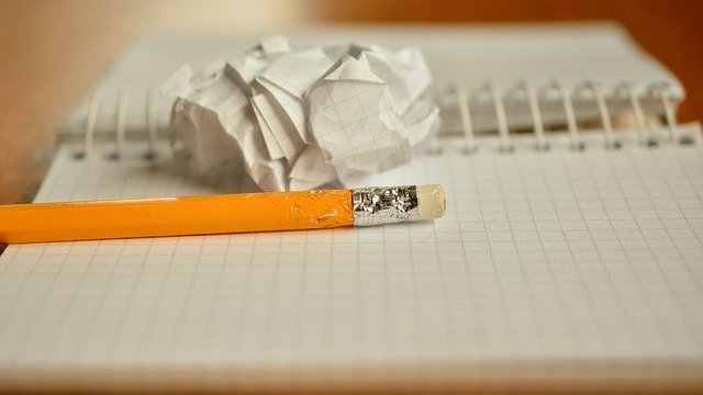 Lápis sobre caderno e folha amassada ao lado