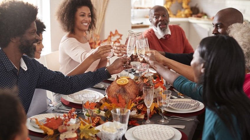 Uma família com várias gerações levantando os copos para fazer um brinde na mesa de jantar.