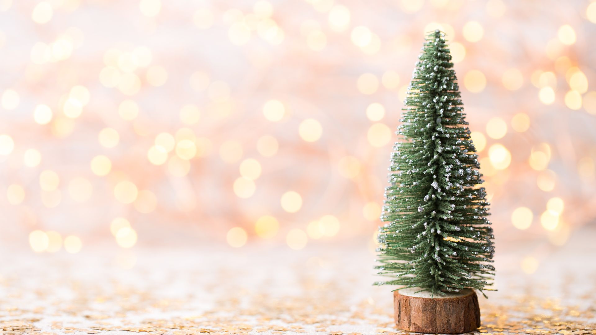 Imagem de fundo dourado e ao lado direito da tela um pinheiro de Natal coberto com flocos de neve.