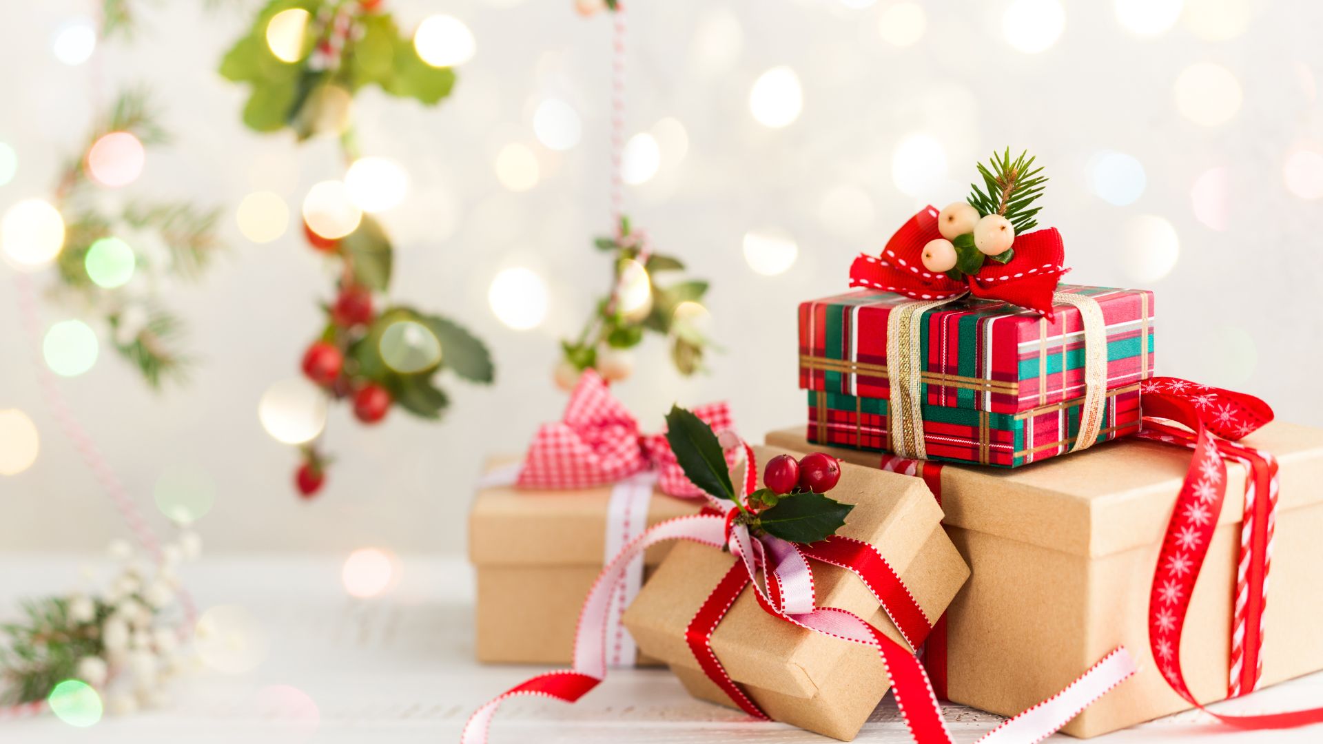 Imagem de fundo branco com luzes dourada. Do lado direito da tela várias caixas de presentes enfeitadas com laços e outros elementos natalinos.
