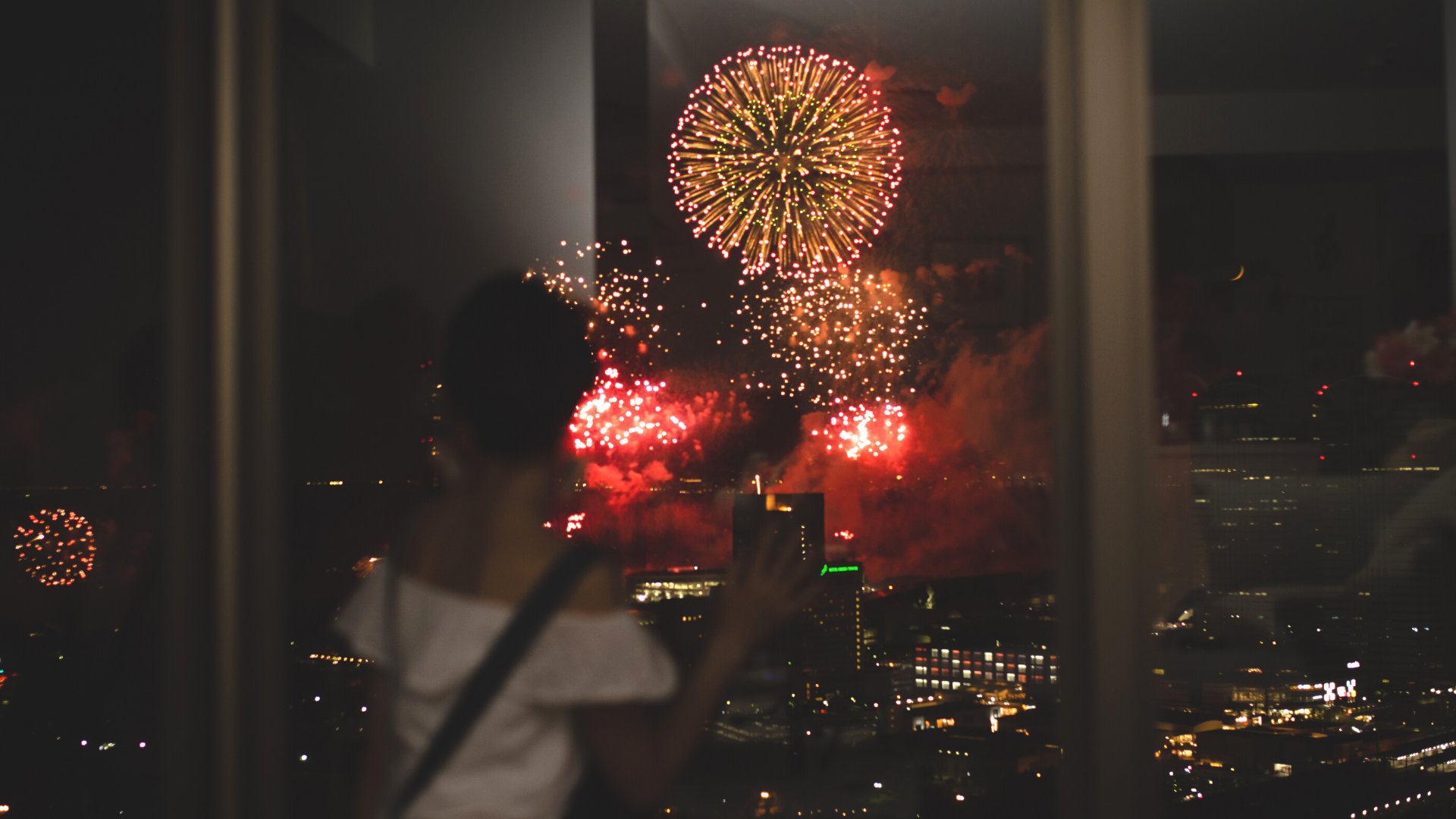 Mulher olhando os fogos de ano novo pela janela de um apartamento