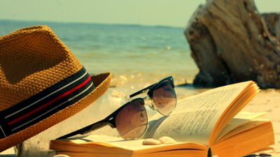 Paisagem de verão com praia, livros, óculos de sol e chapéu.