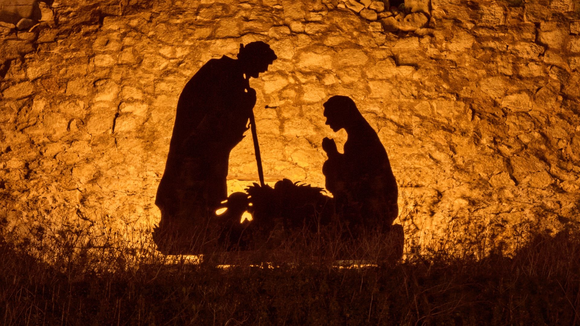 Imagem de fundo dourado que traz a sombra de José e Maria ao lado da manjedoura do menino Jesus.
