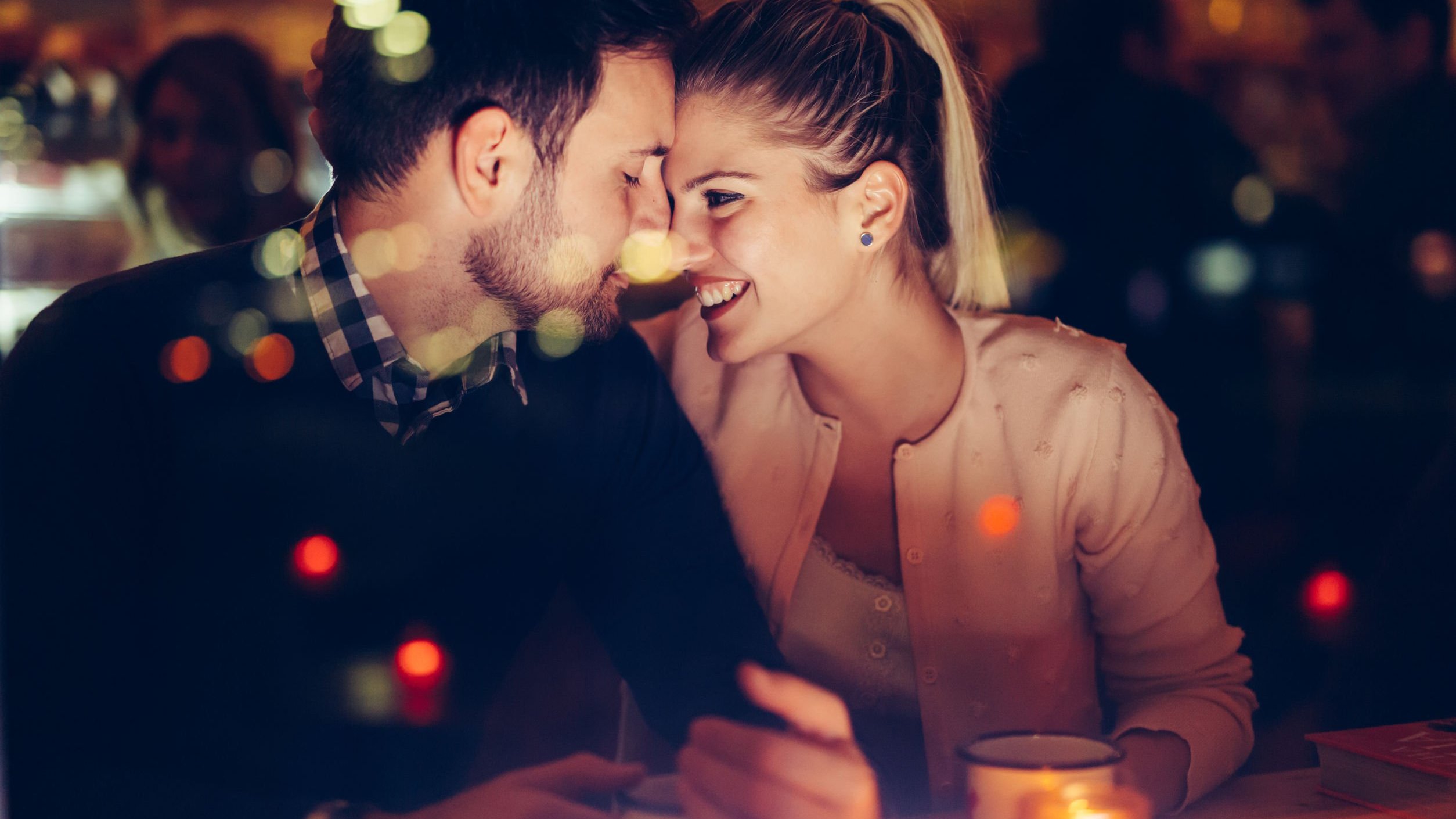 Homem e mulher sentados em um restaurante, com seus rostos encostados.