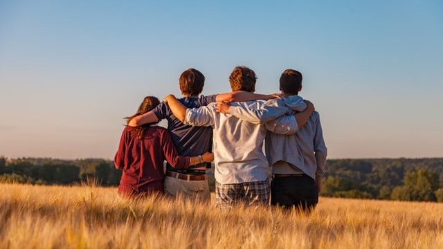 Quatro amigos de costas, abraçados, em um campo