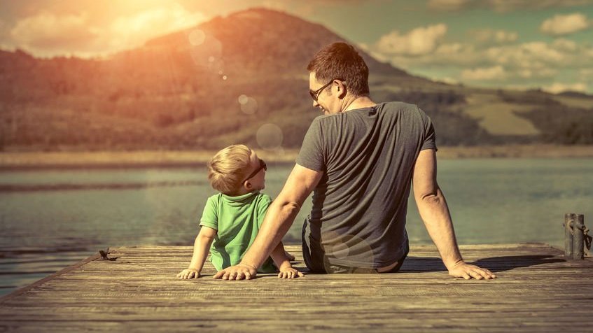 Pai e filho sentados em pier de lago