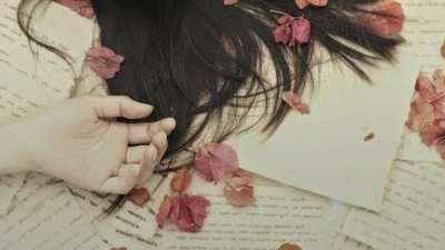 Papéis com manuscrita e flores rosa. O cabelo de alguém que deita sobre os papeis, e a mão de outra pessoa repousando.