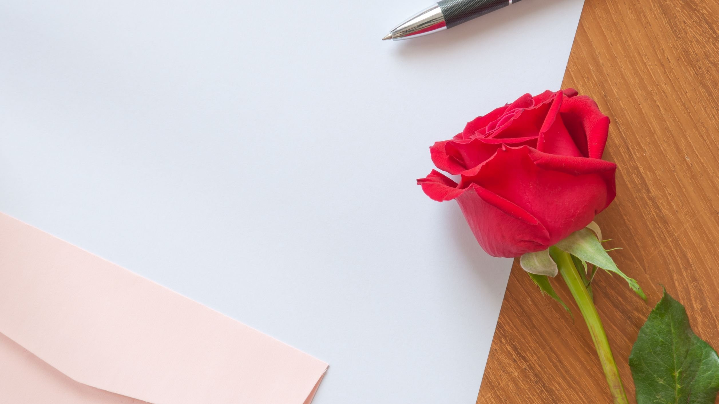 Papel ao lado de uma rosa e caneta