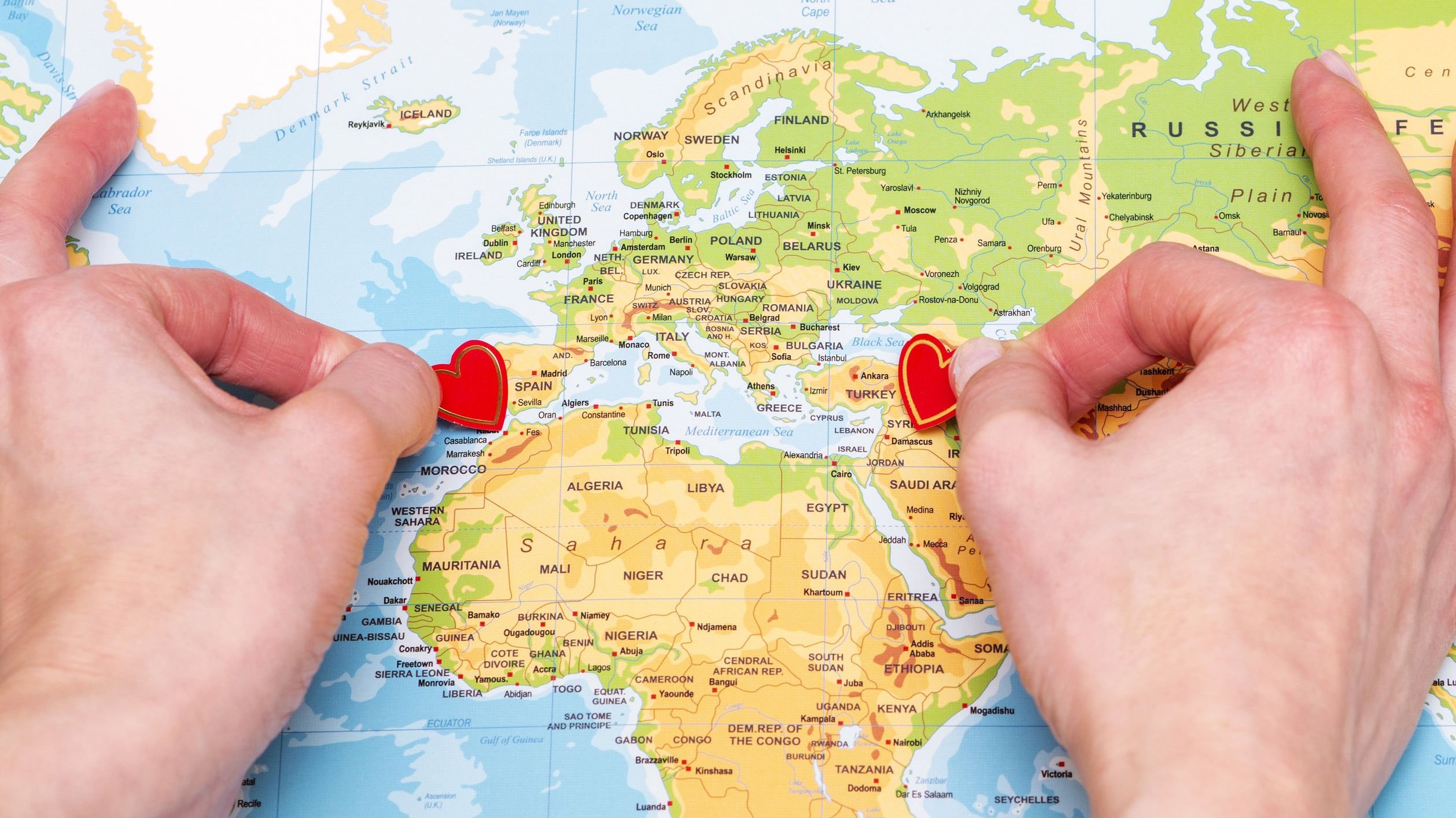 Pessoa colocando dois corações em pontos bem separados em um mapa mundi.