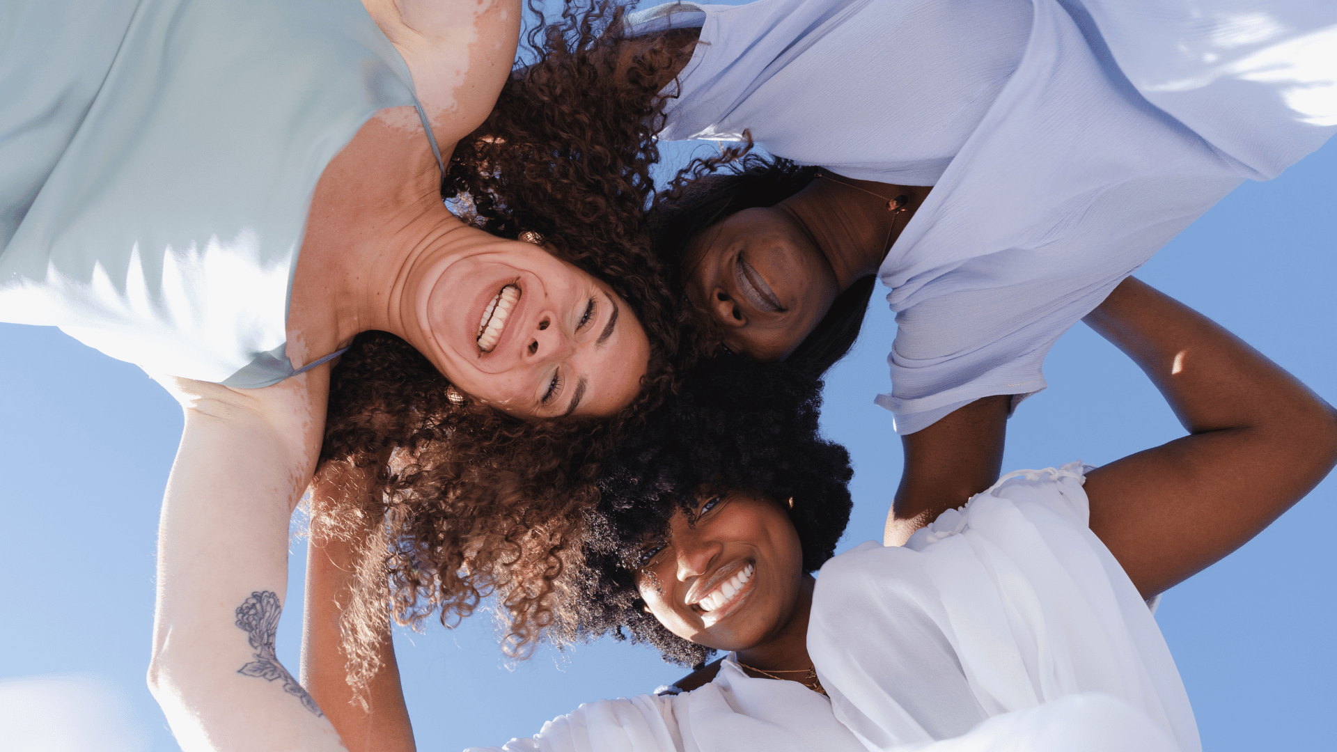 Uma mulher branca e duas mulheres negras se abraçando.