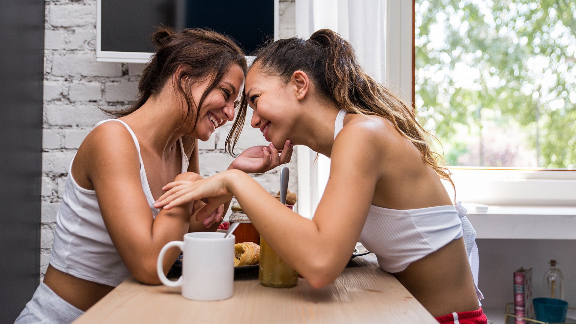 Casal de mulheres sorrindo enquanto dão as mãos durante o café da manhã